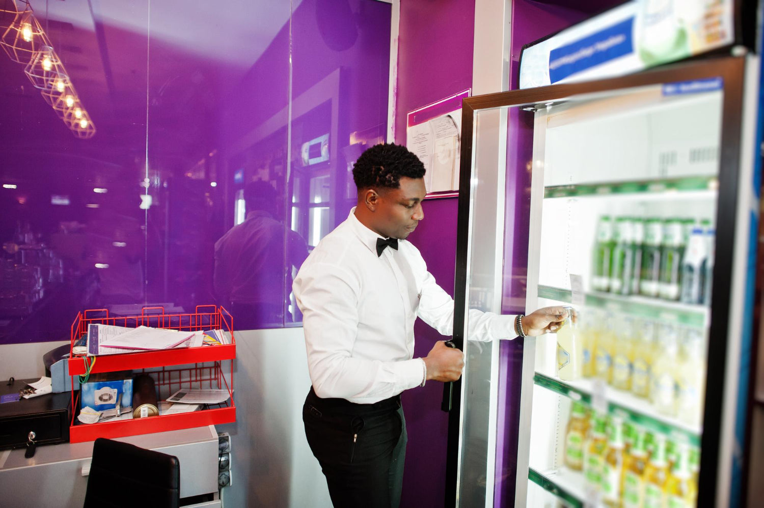 Staff member stocking a glass door drinks fridge in a venue