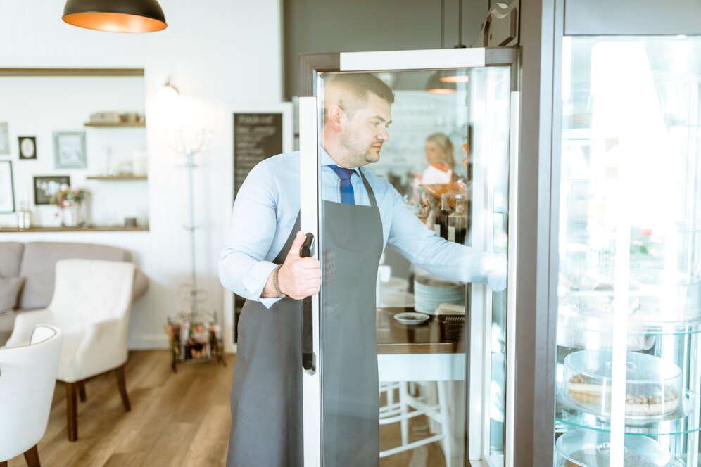 Café owner opening a glass door commercial fridge