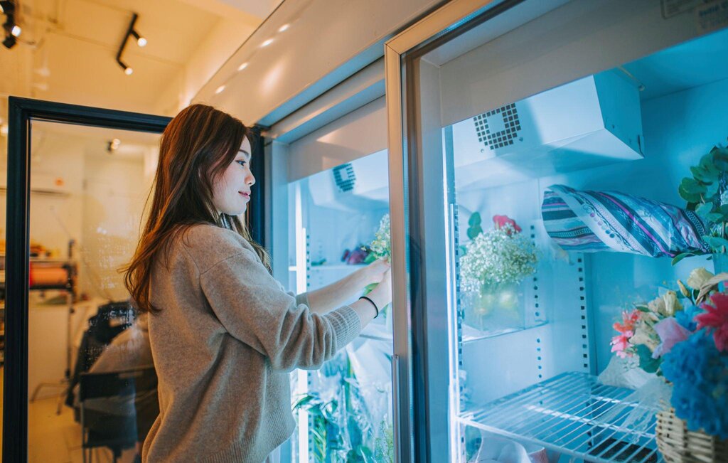 Florist placing flowers into a glass door flower display fridge